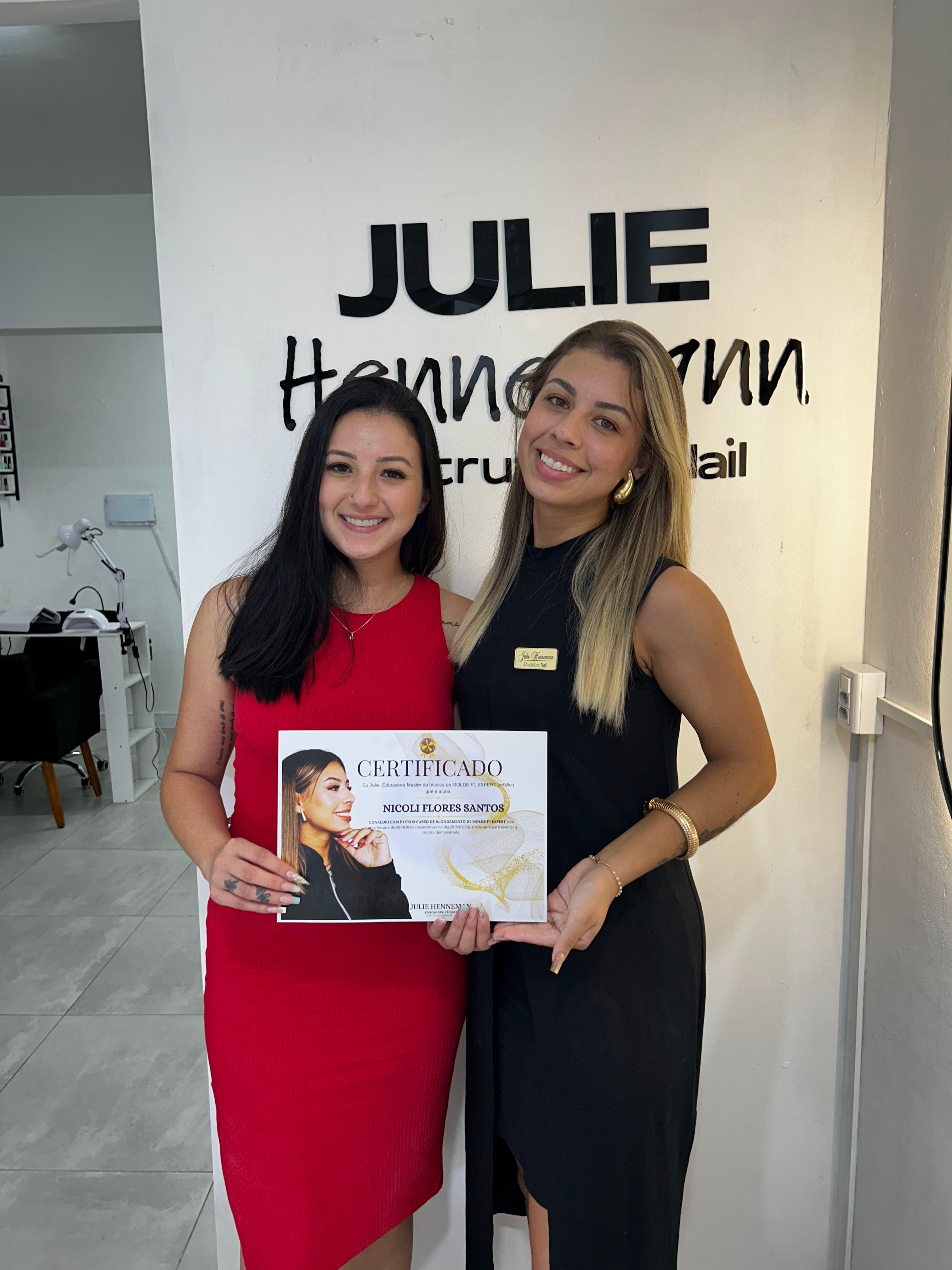 Julie ao lado da aluna Nicoli segurando o certificado de Molde F1 Expert, em frente ao letreiro Julie Hennemann