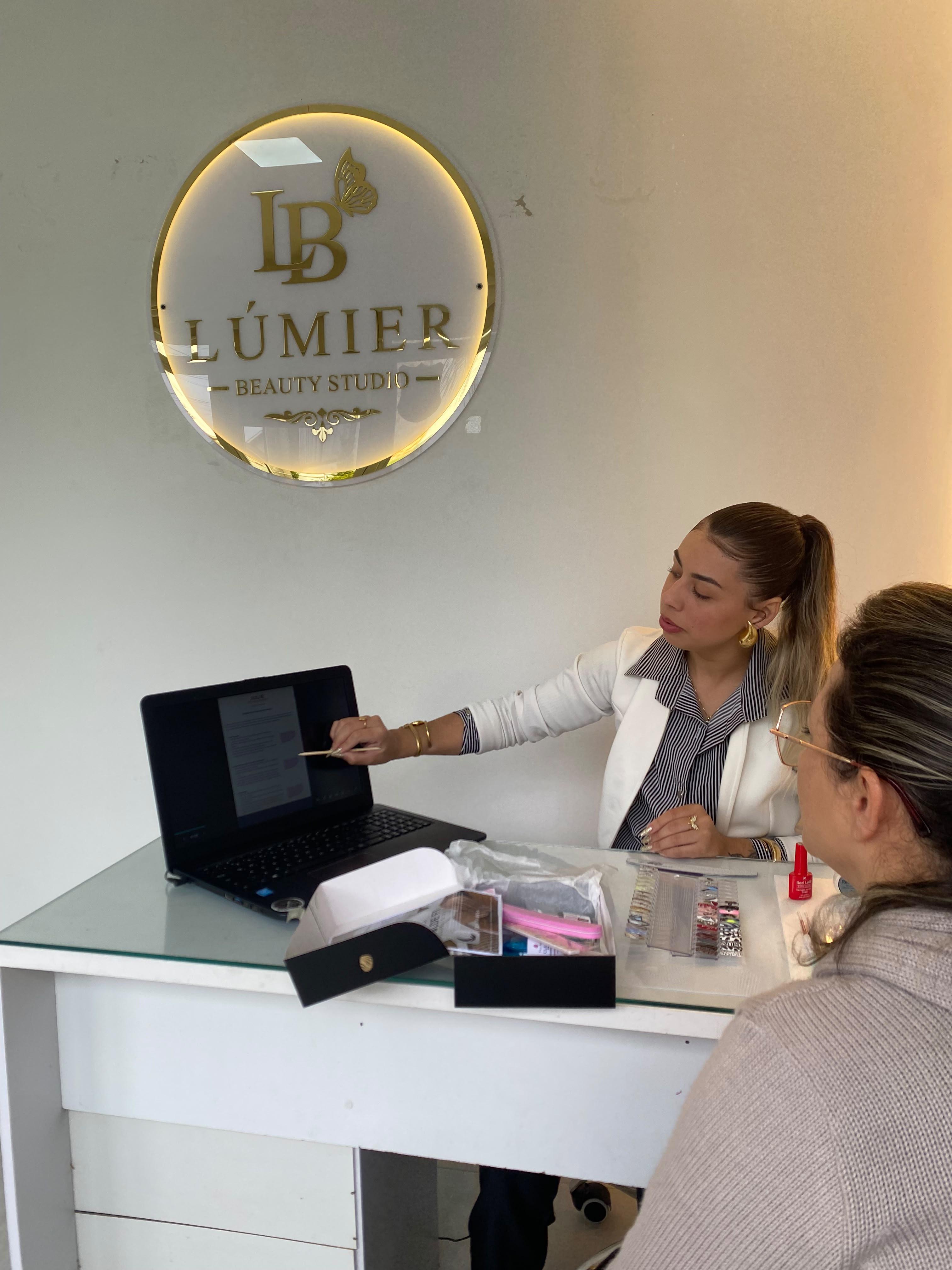 Julie Hennemann explicando o material do curso no notebook para uma aluna no Lúmier Beauty Studio