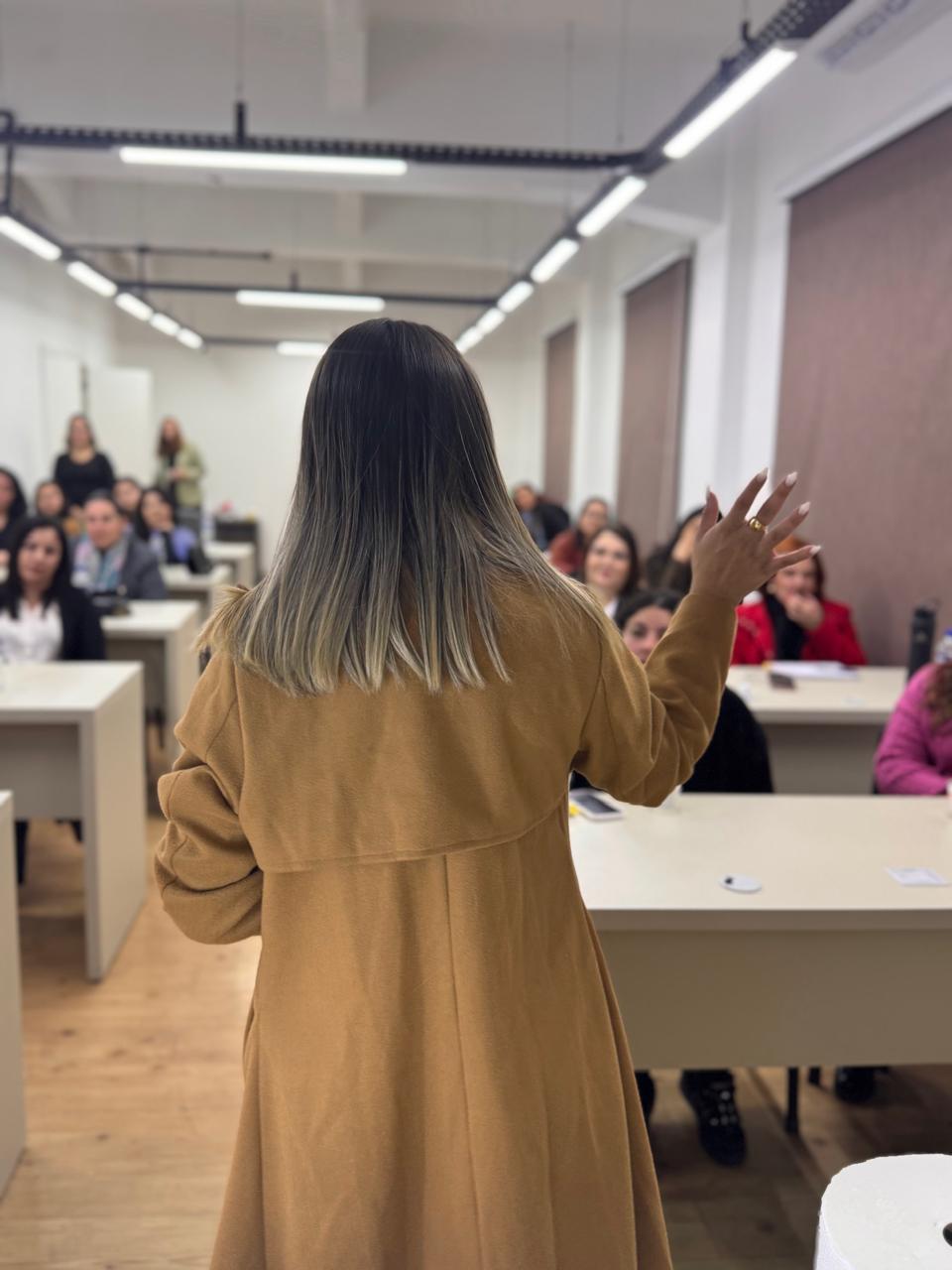 Julie Hennemann de costas falando para uma sala cheia de alunas